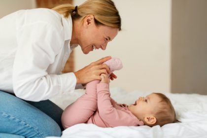 Child care. Happy woman making gymnastics to her baby girl, playing and bonding with infant