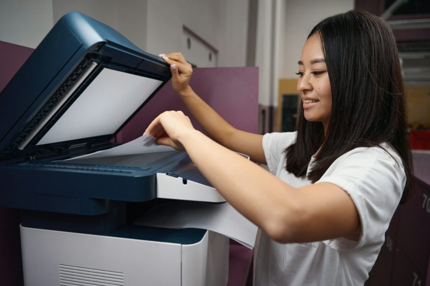 Smiling Asian female is working with printer in modern office