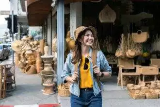 Young female tourist walking across the street and looking at camera while traveling in local market