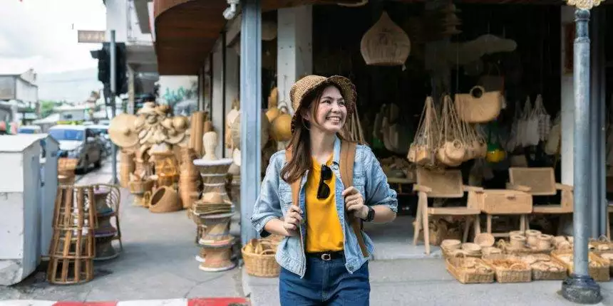 Young female tourist walking across the street and looking at camera while traveling in local market